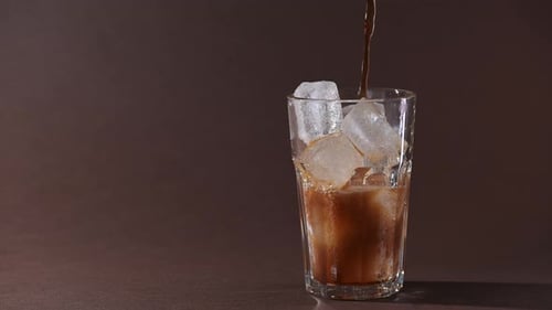 Pouring cola drink with ice cubes close-up.