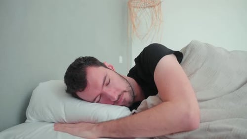 Homme endormi, blanc de race blanche avec barbe, jeune homme couché dans son lit en train de rêver, pi mal à l'aise