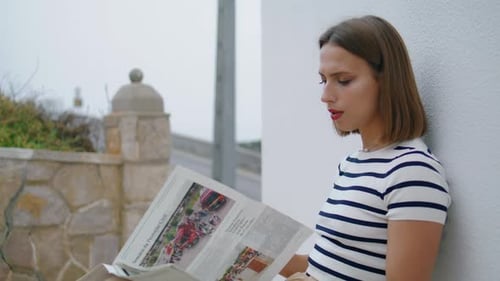 Woman Reading Newspaper By Wall on Overcast Day