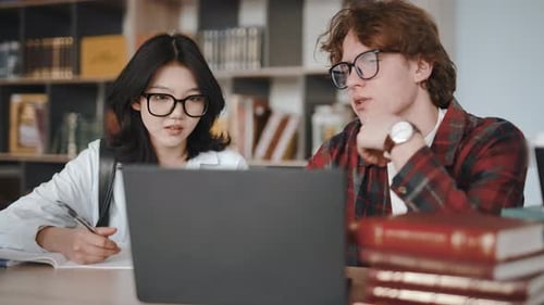 University students discussing a project using a laptop in the library