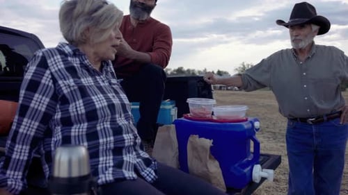 Diverse farmers enjoy lunch break together at pickup truck on rural farm