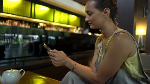 Young woman enjoying coffee and texting on her smartphone in a cozy cafe