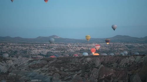 Hot air balloons rise over Cappadocia's rocky landscape at dawn with soft morning light, timelapse