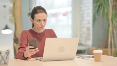 Woman Using Laptop and Phone in Office