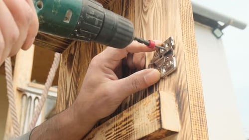 Les mains d'un ouvrier en assemblage de meubles utilisent un tournevis électrique pour fixer la charnière de la porte à un nouveau bois