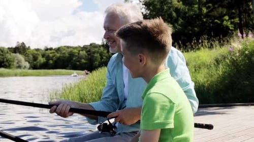 Happy grandfather and grandson enjoying summer fishing on the river berth together