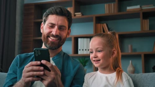 Father and Daughter Look at Mobile Phone and Smile