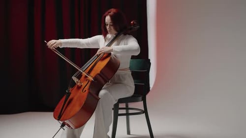 Woman Plays Cello in White Room with Red Curtain