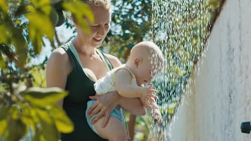 Baby enjoys outdoor summer shower with his mother in the summer garden
