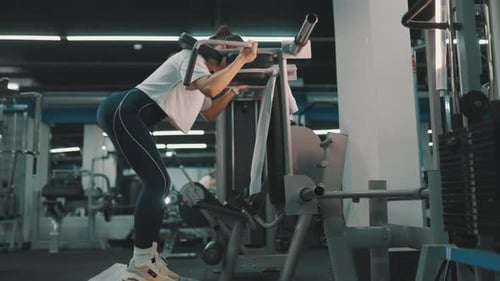 Mulher realizando agachamentos diurnos nas pernas na máquina na academia