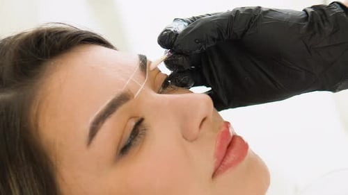 Visagist macht Markierungen mit weißer Paste zum Tätowieren von Augenbrauen