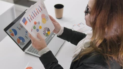 Businesswoman Analyzing Financial Charts and Graphs at Modern Office Desk Reviewing Data Reports for