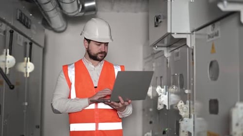 Bearded Worker Uses Laptop in Electrical Room