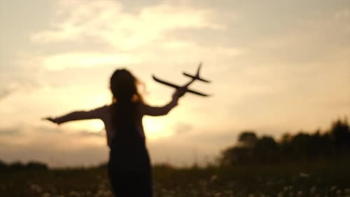 Silhouette of playful little girl run with an airplane on background amazing summer sunset