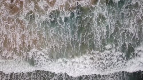 Stormy sea with waves breaking, white foam and beach sand dragged into the sea
