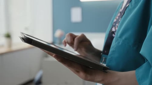 Close-up of Concentrated Young Nurse Using Digital Tablet in Hospital Ward