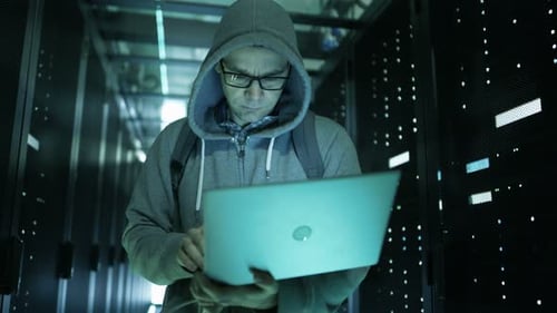Hacker in einem Hoodie, der in der Mitte eines Rechenzentrums voller Rack-Server steht und es mit H hackt