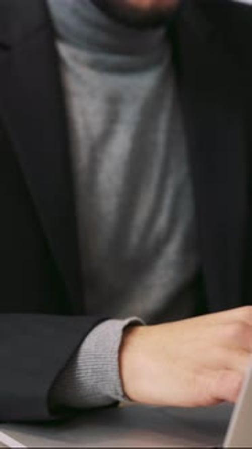 A Suited Man with a Beard Works Intently on a Laptop Showing Professionalism