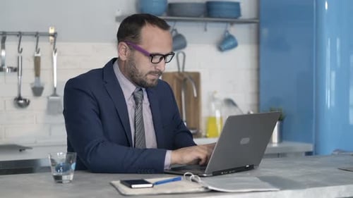 Man in Suit Working on Laptop at Kitchen Counter
