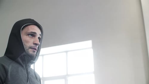 Serious Athlete Wearing Hooded Jacket Walking in Brightly Lit Gym