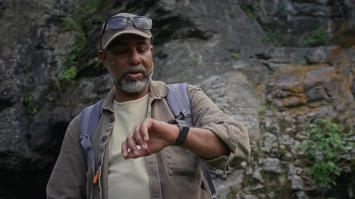 Man with Backpack Looks at Watch in Nature