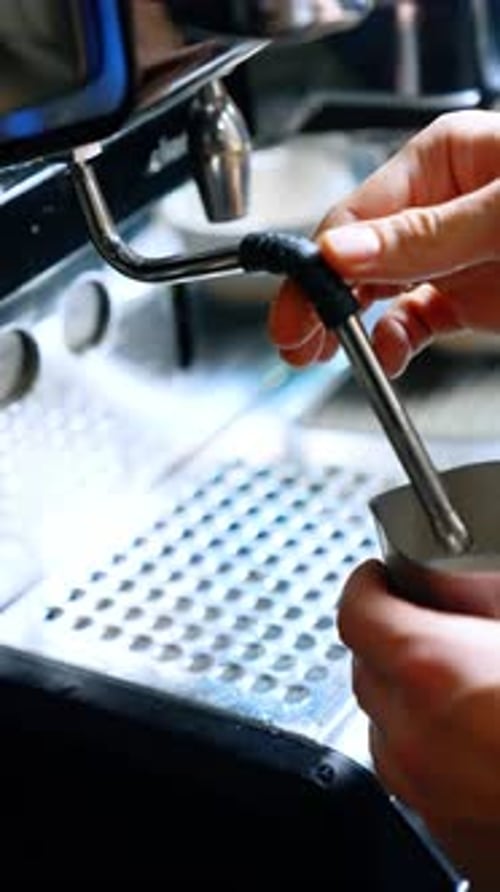 Coffee making machine close up. Male hands hold the pot filling it with hot milk. Close up.