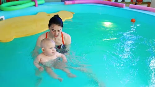 Brunette woman with a little baby in the swimming pool.
