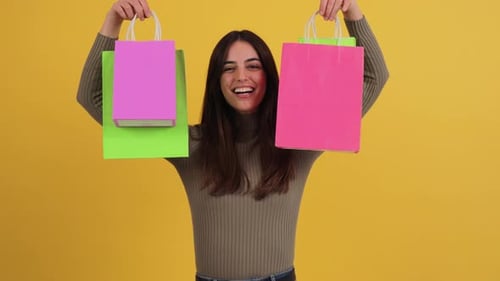 Smiling Woman Holding Colorful Shopping Bags on Yellow