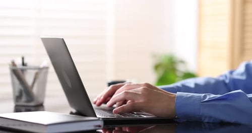 Mann trinkt Kaffee, während er am Schreibtisch im Büro am Laptop arbeitet, Nahaufnahme