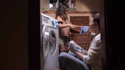 Mutter und Tochter waschen begeistert Wäsche und beladen eine Waschmaschine mit Kleidung von einem