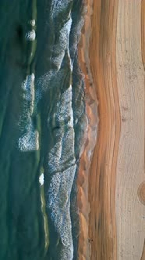 Aerial drone view of waves hitting the shore on the beach in Alicante, Spain. Vertical