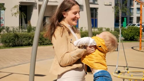 Joli petit garçon souriant et riant alors que sa mère le fait tourner et le fait pivoter sur le terrain de jeu