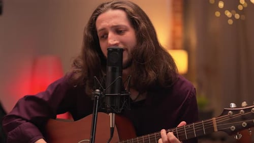 Man with long brown hair playing guitar and singing in home studio