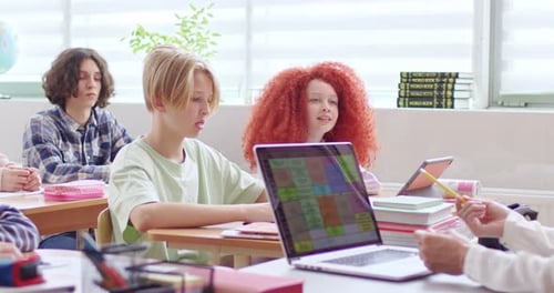 Caucasian Teens Kids Sitting at Desks in School and Rising Hands Up When Teacher Asking Smart