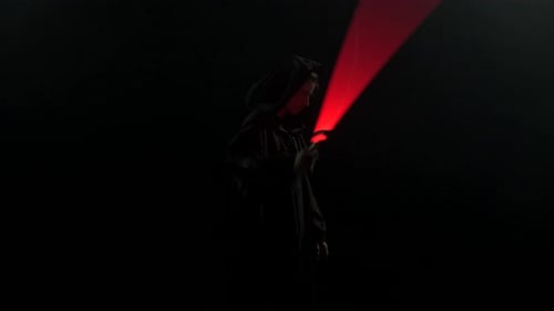 Young Man in Jedi Cosplay Costume with Lightsaber Battle on Black Background in Smoke and Rain Slow