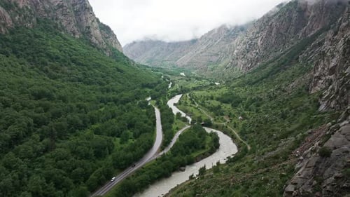 Winding Mountain Road Following River Through Green Valley