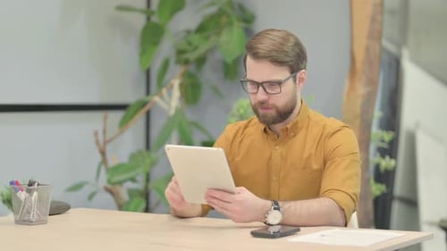 Man at Desk Celebrates Success on Tablet