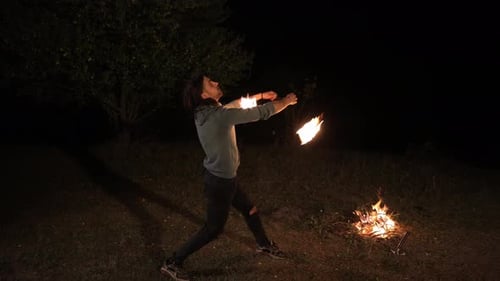 Man Juggling Fire Sticks at Night by Campfire