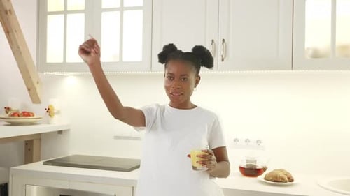 Woman Dancing Happily in Bright Kitchen with Juice