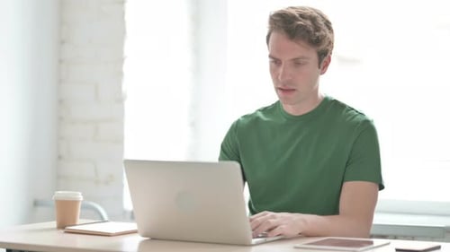 Young Man Celebrating Online Success on Laptop in Office