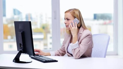 Woman works at computer and talks on phone