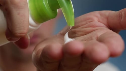 Young Man Squeezing a White Moisturizer From a Tube on His Hand Closeup Morning Routine Beauty and