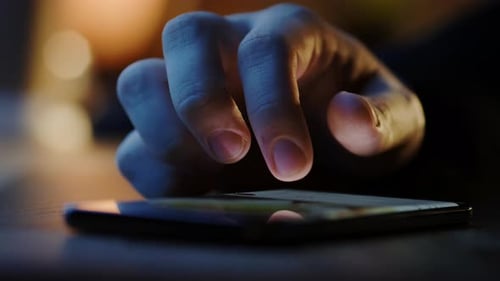 Hand scrolling on cell phone at night close-up