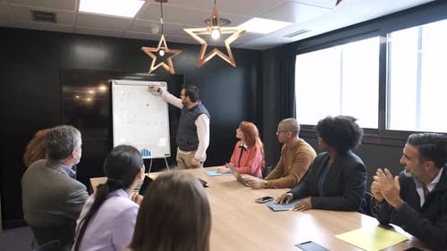 Businessman Explaining Strategy on Whiteboard to Diverse Colleagues in Office