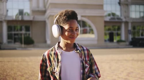 Smiling Child with Headphones Stands Outside Building