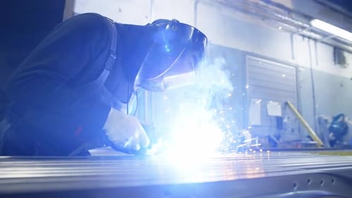 Der Mann arbeitet als Schweißer in der Fabrik, er trägt besondere Kleidung