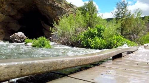 Rushing water is seen flowing over a bridge. A cavern is seen above it.