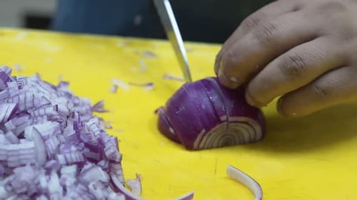 Close-up of hands chopping red onion on a yellow cutting board, kitchen setting