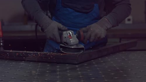 Worker uses angle grinder on metal frame with sparks