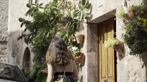 Video of a Young Woman Walking in Slow Motion Next to a Stone House with a Vertical Garden